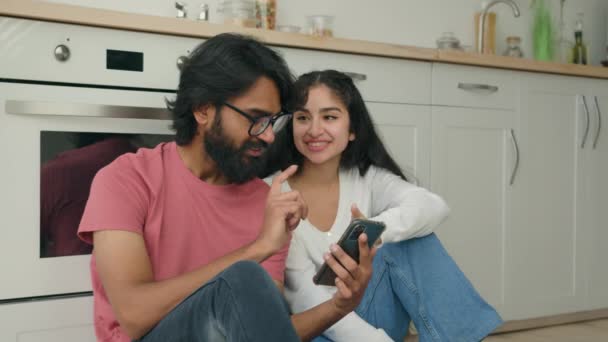Multiracial Ethnic Couple Sit Floor Kitchen Use Smartphone Application Watch — Vídeo de Stock
