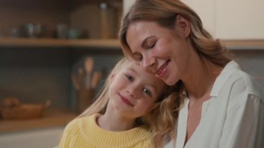 Portrait Caucasian preschool cute affectionate adopted little girl child daughter schoolgirl hugging foster cuddle care mother with eyes cuddling mum cuddling kid enjoy tender sweet moment at kitchen
