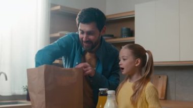 Caucasian family adult father dad with kid child girl little daughter standing in kitchen unpack paper shopping bag with food vegetables get out fresh natural products e-store delivery services online