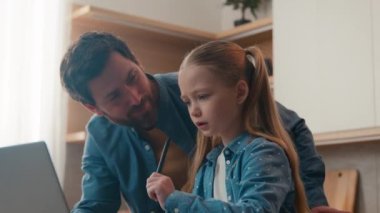 Caucasian bearded father helping cute school child daughter with homework studies sit at kitchen table with laptop. Dad explaining help kid girl distance learning at home. Primary quarantine education