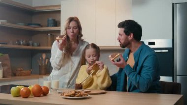 Kafkasyalı mutlu bir aile mutfakta birlikte kahvaltı ediyor. Neşeli ebeveynler ve tatlı küçük kız evde birlikte akşam yemeği yerken çikolatalı sandviçle ekmek yiyorlar. Anne, baba ve kız yemek yiyor.