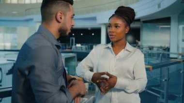 Diverse colleagues multiethnic multiracial coworkers talking in company office. African American woman businesswoman and Arabian Indian man businessman talk speak conversation discuss in business hall