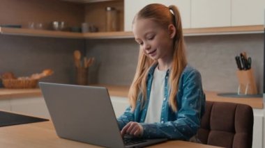 Kafkasyalı küçük kız, ev mutfağında dizüstü bilgisayar eğitimi kursu ödevini online olarak kullanıyor. Öğrenci kız öğrenci öğrenci, internet tarayıcı uzaklık ağı öğreniyor.