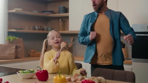 有趣的白胡子父亲跳舞滑稽的舞姿 而小女孩小女孩用勺子唱歌 就像厨房里的话筒唱卡拉Ok — 图库视频影像