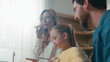 Hareket eden beyaz kız çocuğu çocuk anne ve babaya kahvaltı hazırlamak için ekmeklere çikolata ezmesi sürdü. Aile, mutfakta birlikte öğle yemeği yiyor. Evdeki masada yemek yiyor.