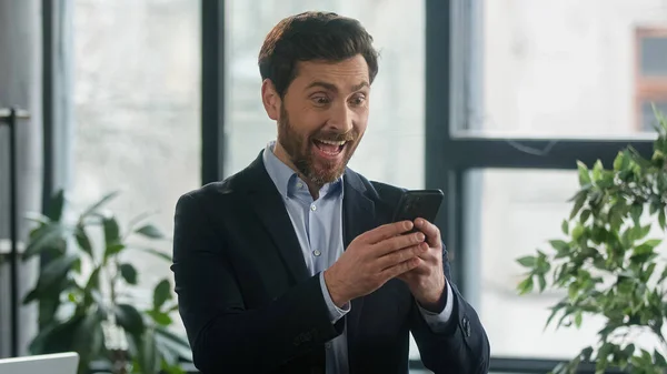 Surprised happy caucasian man winner reading good news on mobile phone feel amazed overjoyed excited businessman win online auction career advancement holding smartphone receiving winning notification