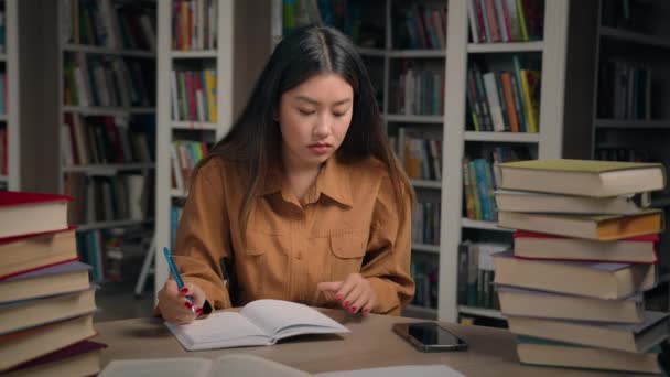Ασιάτισσα Μαθήτρια Που Κάθεται Στη Βιβλιοθήκη Γράφει Κάνοντας Την Εργασία — Αρχείο Βίντεο