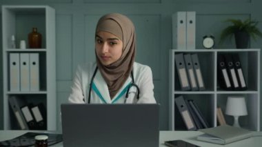 Doctor arabian islamic ethnic woman female medic psychologist talking provide video call on laptop professional medical support to client remote physician speak in conference application at hospital