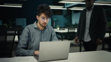 İki farklı etnik işadamı online iş projesini dizüstü bilgisayarla tartışıyor. Kızgın Afrikalı patron Hintli stajyere işinde yardım ediyor Amerikalı lider ofiste çok ırklı takım ortaklığı öğretiyor.
