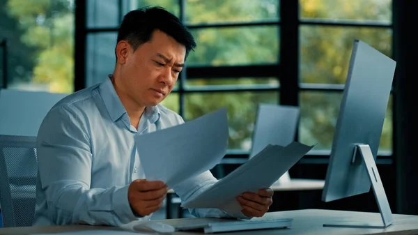 Disappointed angry Asian office manager mature man specialist lawyer banker work with paper documentation read legal documents check error bankruptcy problem negative incorrect result business failure