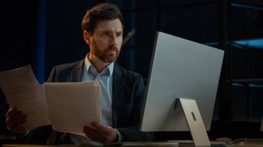 Konsantre Kafkasyalı avukat belgelerle çalışıyor iş belgelerini okuyor finansal kağıt sözleşmelerini kontrol ediyor kredi faturalarını ödeyen yetişkin erkek işadamı denetleyici online bilgisayar bankacılığı uygulaması kullanıyor