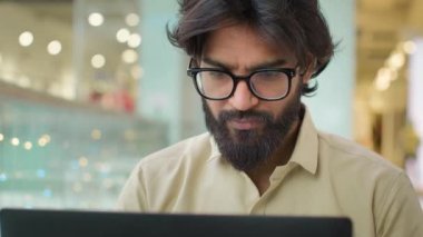 Indian Arabian bearded business man entrepreneur in glasses typing on laptop male professional businessman using computer sitting at office showing ok gesture okay good online service excellent work