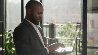 Bilgisayarlı internet sitesinde dizüstü bilgisayarı güneş ışınlarında yazan olgun bir adam. Orta yaşlı Afrikalı Amerikalı etnik iş adamı erkek yönetici modern ofiste çalışan dijital verileri arıyor