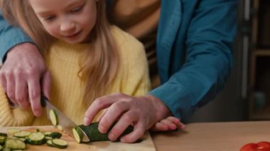 Loving father teach daughter girl cook holding knife cutting fresh vegetable salad in kitchen prepare healthy meal dad take care of child safety at kitchen learn to cut cucumber under daddy control