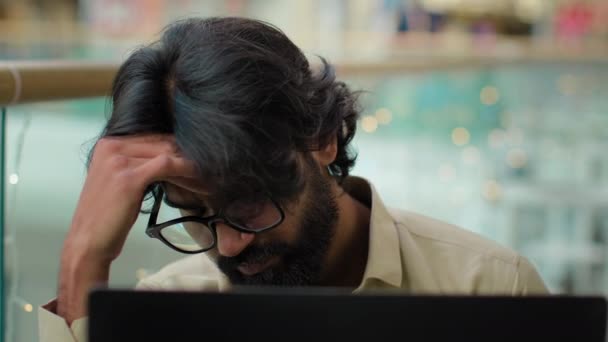 筋肉の緊張の頭痛の痛みを伴う頭の痛みを伴う頭の中で苦しんで眼鏡でインドのひげを生やした男は コンピュータ作業で過労した 疲れたアラビア人のビジネスマンはラップトップのオフィスでの問題に圧倒されました — ストック動画