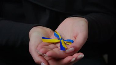 Close-up unrecognizable female and male hands hold blue yellow ribbon family couple volunteers palms holding ukrainian symbol stand with Ukraine protection charity support victims of war cropped view