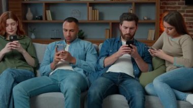 Dört farklı Afrika kökenli beyaz Amerikalı arkadaş oturma odasındaki koltukta oturup mobil ekrana bakıyorlar telefon zımbırtıları internetteki erkekler birbirlerini umursamıyorlar.