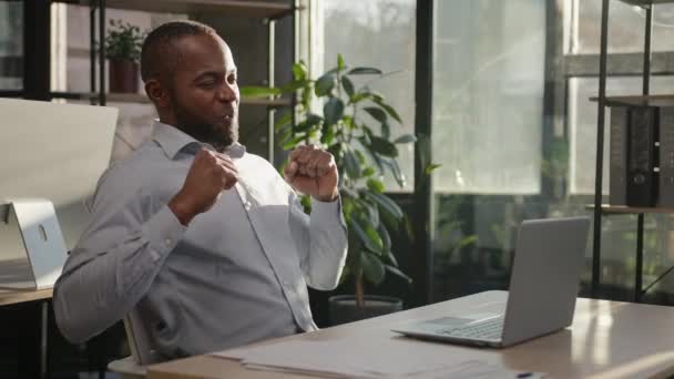 面白いアフリカのビジネスマン成熟した民族の中年40代の男性マネージャーCeoエージェントは 日当たりの良いオフィスでデスクアメリカの大人の労働者で踊るラップトップコンピュータ上でオンライン勝利を祝う — ストック動画