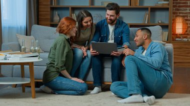 Multiracial team friends ethnicity diversity shoppers sit in living room work with laptop use credit card for online payment ordering delivery service spending money finances internet shopping talking