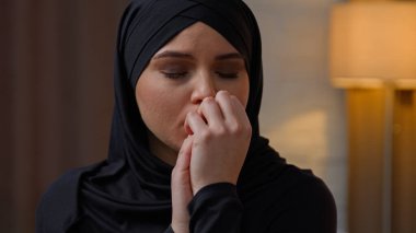 Üzgün, üzgün, ağlayan Arap, Müslüman kadın, çok ırklı, evde oturan, endişeli kız arkadaş, yalnız başına, ayrılık krizi, sağlık sorunu ve keder yüzünden üzülüyor.