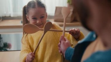 Unrecognizable dad father man and little daughter fighting with spoons in kitchen having fun while cooking together. Unknown daddy with child kid girl funny fight battle at breakfast family at table
