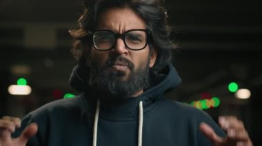 Male portrait at dark parking lot irritated emotional angry Indian bearded man in glasses shouting screaming yelling with mad anger aggressive Arabian guy shout scream to camera with furious stress