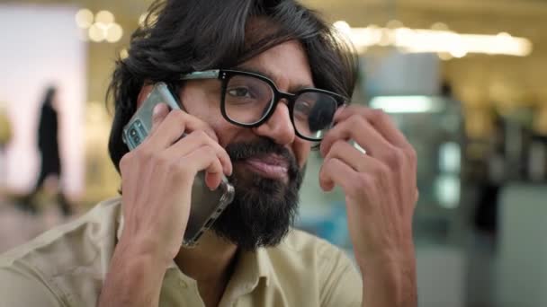 把戴着眼镜的印度大胡子男子关在室内与朋友交谈 用手机笑着 阿拉伯人用智能手机远程解决商业交易微笑的商人讲手机 — 图库视频影像