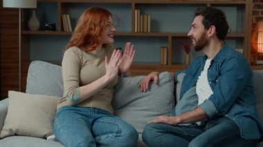 Woman talking with man at home joyful Caucasian couple sit on couch redhead girl telling funny story positive diverse partners laughing with joke having fun laugh discussing news friendly talk on date