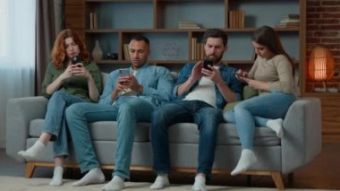 Grup arkadaşları kanepeye oturup cep telefonlarıyla sosyal medyada sohbet ediyorlar. Birbirlerini görmezden geliyorlar. Çok ırklı kadınlar ve erkekler çeşitli aletler kullanıyorlar.