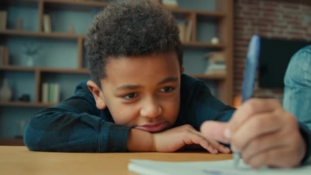 怠惰やる気のない疲れ疲れ少しアフリカ系アメリカ人の生徒の少年ノートをテーブルの上に横たわって宿題を書いて書きます エスニック子男の子子供息子で机書きでコピーブック退屈なクラスレッスン — ストック動画