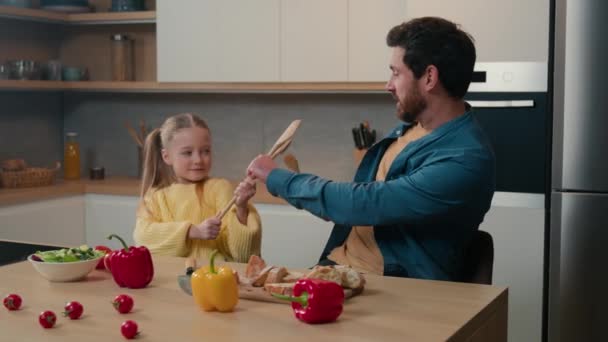 白人家庭在厨房里 成年男子父亲和小女儿在一起做饭 一边和勺子打斗 一边一起吃饭 爸爸和小孩女孩打斗打斗打斗 — 图库视频影像
