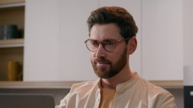 Bilgisayarlı beyaz bir adam evde çalışıyor. Serbest çalışan bir iş adamı. Kameraya gülümsüyor. Erkek müşteri mutfaktaki gülümsemede bilgisayarla yemek siparişi veriyor. Pozitif ev sahibi kiracı