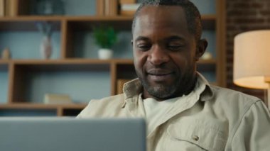 Yakın plan Afro-Amerikalı adam dizüstü bilgisayarında e-postalarını kontrol ediyor mesajları tarıyor sosyal ağ sohbetleri kuruyor online mağazada sipariş veriyor internet üzerinde çalışan olgun iş adamı serbest çalışıyor.