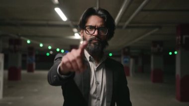 Yakın plan ciddi Hintli HR yöneticisi iş başvurusu için adayını seçiyor kamerayı davetkar yapıyor buraya gelip yeraltı otoparkında duran etnik genç işadamını işaret ediyor.