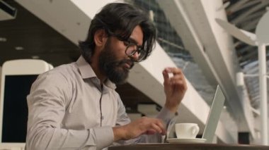 Pensive Indian businessman typing on laptop remote working internet concentrated arabian man manager analyzing digital data create business plan using computer app indoors send email in social network
