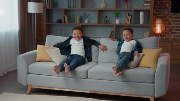 幸せな家族2つの養子アフリカ系アメリカ人の少年たちの子供たちの兄弟子供たち一緒にリラックスしたリビングルームでリラックスソファ笑いリラックス居心地の良いソファ保育幼少期に横たわって — ストック動画