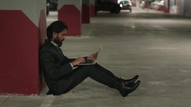 绝望的印度失业男子坐在地下停车场 在笔记本电脑上浏览社交网络 用计算机应用程序在网上寻找工作的无家可归的阿拉伯不幸商人 — 图库视频影像