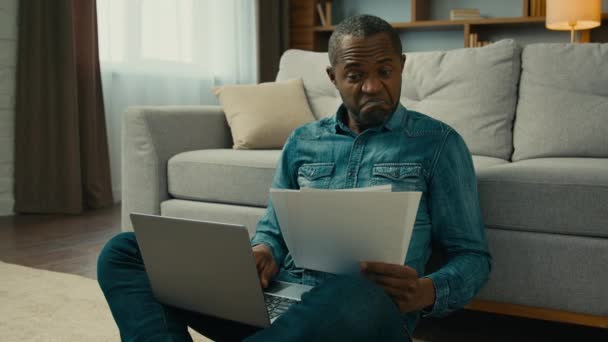 Здивований Зрілий Афроамериканець Вводить Дані Ноутбук Паперових Документів Задоволених Річним — стокове відео