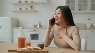 Şaşırtıcı Asyalı Japon kadın evcil mutfakta cep telefonuyla konuşuyor. Arkadaşlarıyla konuşuyor. İyi haberler, dedikodu, etnik çeşitlilikte ev hanımı, cep telefonuyla konuşuyor.