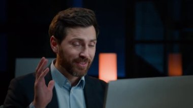 Akşam iş konferansı çağrısı. Karanlık ofisteki 30 'lu yaşlardaki adam internet kamerası görüntülü sohbet brifinglerine bakın. İnternette yetişkin beyaz iş adamı Webinar eğitimi alıyor.