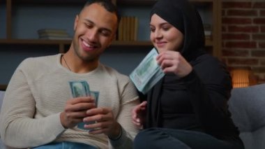 Değişik etnik çiftler koltukta oturup para sayıyor. Banknotlar, Afro-Amerikan erkek koca tesettürlü Müslüman eşlere para veriyor. Aile bütçesi, zengin ortaklar nakit para sayıyor.