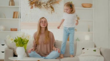 Nilüfer pozisyonunda meditasyon yapan, düşünceli, bekâr, beyaz, sakin bir anne. Yoga egzersizi yapıyor. Evdeki kanepede oturuyor.