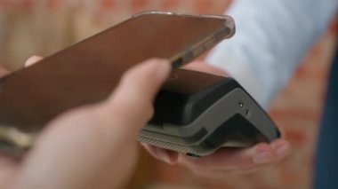 Yakın plan kadın elleri, NFC teknolojisini akıllı telefon kız müşterilerinde kullanan tanınmayan kadın müşteriler için, banka terminali üzerinden ödeme yapmak için cep telefonu kullanıyor.