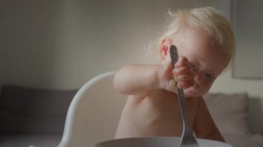 Komik küçük kız çocuk, çatallı yulaf lapasıyla yer kendi gülüşüyle beyaz kız bebek bebek bebekle çocuk yuvasında yüksek beslenme sandalyesinde çocuklar için sağlıklı yemek yiyebilir.