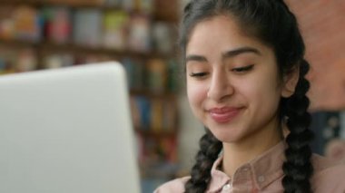 Kapalı alanda dizüstü bilgisayar ekranına bakan gülümseyen genç Hintli kadın e-postaları kontrol eden sosyal ağ araştırması yapan İspanyol kız öğrenci çevrimiçi uzaktan kumandada sohbet ederek bilgisayardan mesaj yazıyor.