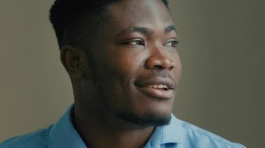 Etnik afro-amerikan yetişkin 30 'lu yaşların iş portresi iş adamı ofis CEO' su gri arka planda hayal kuran erkek yüzü kameraya bakıp gülümseyen dişlek adama bakıyor.