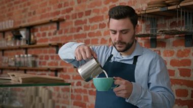 Kafeteryadaki tezgahta kahve yapan Kafkasyalı garson garson barmen Barista lezzetli kapuçino hazırlayan profesyonel barmen çalışanı müşteri siparişini kameraya bakıp gülümsetiyor.