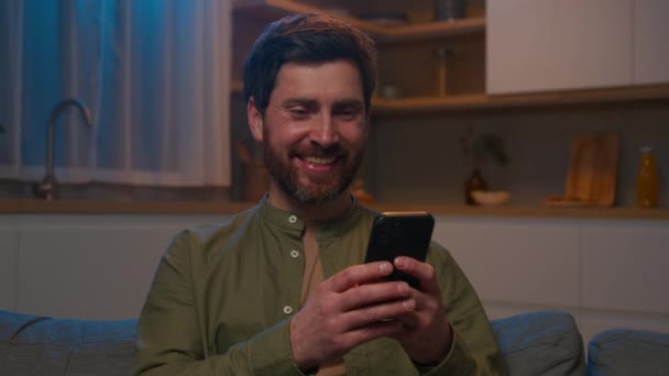 Счастливый Улыбающийся Кавказский Мужчина Помощью Мобильного Приложения Телефоне Отдыхает Диване — стоковое видео