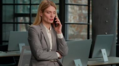Yetişkin, beyaz, 40 'lı yaşlarda profesyonel bir kadın cep telefonuyla konuşuyor. İş telefonuyla ciddi bir iş görüşmesi var. Ofiste orta yaşlı bir iş kadınının konuşma mesafesinde.