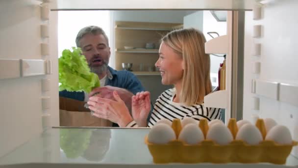 冷蔵庫の中からの視点中年夫婦の配偶者からのハメ撮り冷蔵庫の棚に製品を置く紙袋から野菜料理を取る成人男性と女性の夫と妻 健康的な栄養 — ストック動画